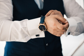 primo piano di un uomo  vestito in giacca e cravatta che sistema il suo orologio da polso 