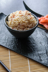 Brown rice served in a black bowl on a wooden mat.