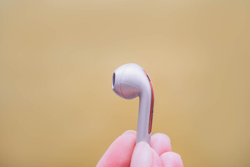 Close up of hand holding golden beige bluetooth earphones or wireless earbuds isolated on beige...