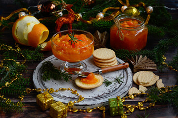 Fototapeta na wymiar Glass jar of orange jam and New Year's decor on a dark wooden table.