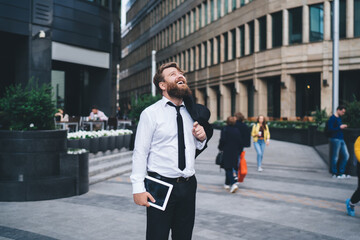 Cheerful businessman with tablet standing on street