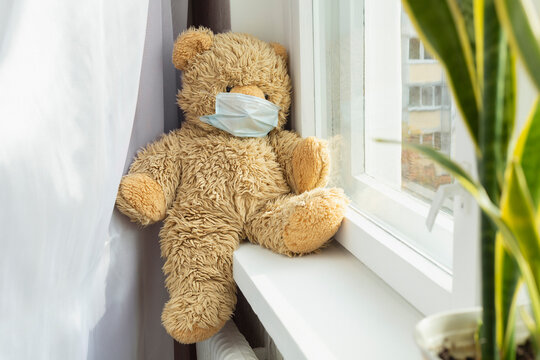 Cute teddy bear in protective face mask on windowsill
