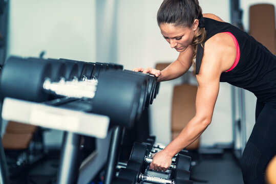 Woman Lifting Dumbbell From Rack In Gym