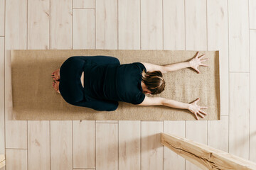 Top view of woman woman practicing yoga indoor. Woman curls up and stretches forward. Fitness female on exercise mat over light floors.