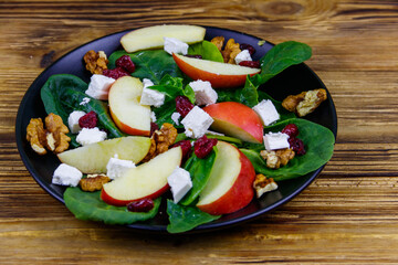 Autumn spinach salad with apple, feta cheese, walnut and dried cranberry on wooden table. Healthy vegetarian food