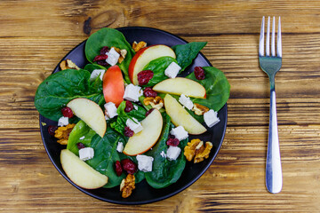 Autumn spinach salad with apple, feta cheese, walnut and dried cranberry on wooden table. Top view. Healthy vegetarian food