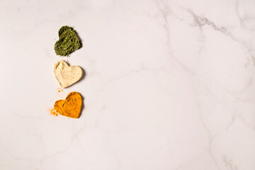 Top view of Three heart shapes of spices on Light Marble background. Heart silhouettes of dried basil, ginger and turmeric powder. Spicy love symbols. Little hearts on marble kitchen table. Still life