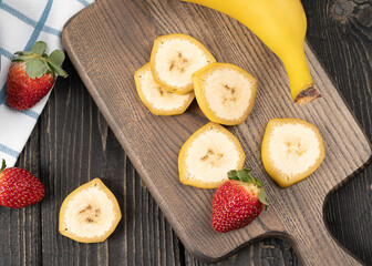 Naklejka na ściany i meble Sliced bananas with strawberries on a wooden desk close up 