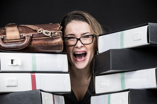 Segretaria  bionda con occhiali da vista, vestita con  di nero e disperata e preoccupata in mezzo a tutti i documento disordinati del suo ufficio  , isolata su sfondo nero