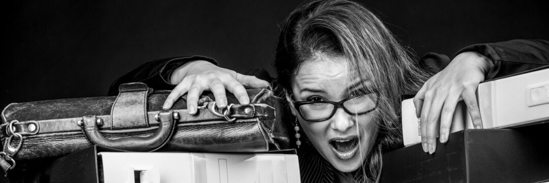 Segretaria  bionda con occhiali da vista, vestita con  di nero e disperata e preoccupata in mezzo a tutti i documento disordinati del suo ufficio  , isolata su sfondo nero