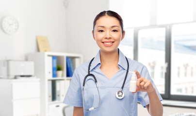 medicine, profession and healthcare concept - happy smiling asian female doctor or nurse in blue uniform with stethoscope and oral spray over hospital background