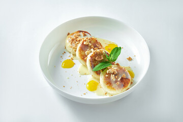 Delicious Ukrainian breakfast - cheesecakes with nuts, mango and white sweet sauce in a white plate. on white background. Syrniki