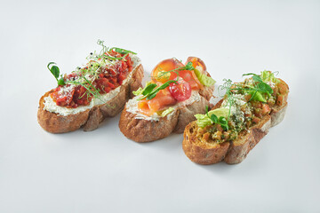 Italian appetizer - three bruschetta with tomatoes, salmon and baked peppers on a white background