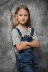 girl child in a gray t-shirt and denim overalls on the background of an old wall