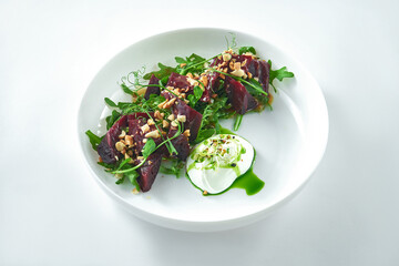 Appetizing and dietary salad of baked beetroot, arugula and microgreen with green butter and white sauce (feta cheese mousom) in a white plate.