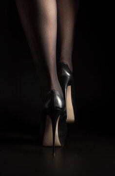 Legs of a woman in high heels in black tights on a black background. Side view with space to copy.