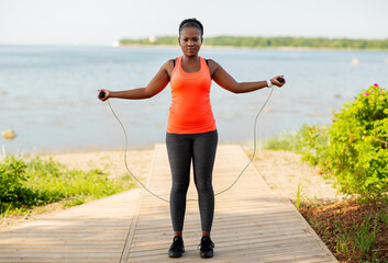 fitness, sport, training, park and lifestyle concept - african american woman exercising with jump...