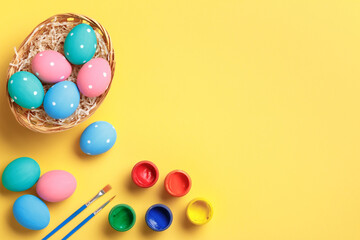 Happy easter. Multi-colored eggs in a basket, brushes and paints on a yellow background. Flat lay greeting card with copy space.