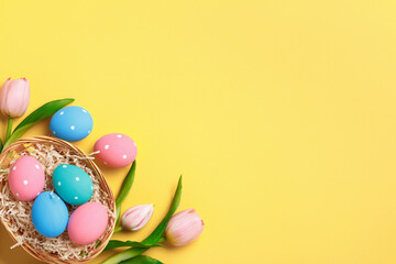 Easter greeting card invitation. Multi-colored painted eggs in a basket, pink tulips on a yellow background.