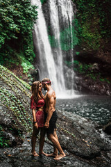 Fototapeta na wymiar A couple in love on a waterfall. Honeymoon trip. Happy couple on the island of Bali. Beautiful couple travels the world. Travel to Indonesia. Happy couple on vacation. Wedding trip. Copy space