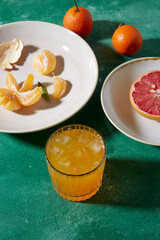 food, healthy eating and fruits concept - still life with mandarins, grapefruit and glass of juice on green background