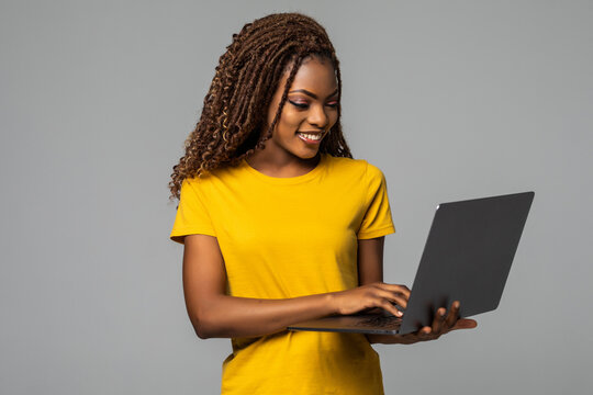 Young smiling african woman standing with laptop computer isolated on gray background