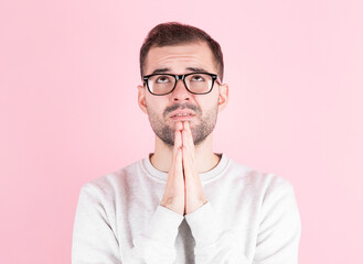 Picture of young man isolated on pink background, having put hands together in prayer, wishing dreaming and waiting for all best