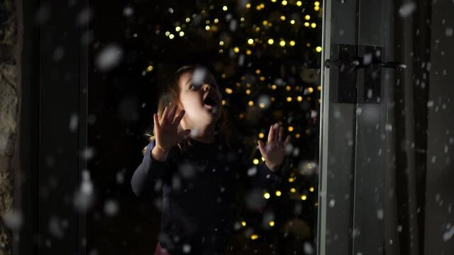 4K: Child looking through Window at Christmas watching the Snow falling outside. Christmas Tree behind. Stock Video Clip Footage