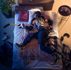 Attacking. Top view of young professional hockey player sleeping at his bedroom in sportwear with equipment. Loving his sport, workaholic, playing match even if resting. Action, motion, humor.