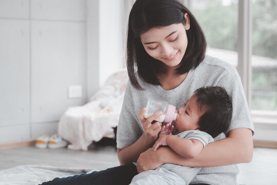 Young asian mother feeding baby from milk bottle.