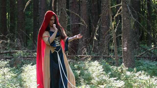 A girl in a red cloak in the forest among the trees. Moves his hands. Does the magic of hand movements. The Forest Witch