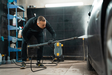 Professional car wash. Detailing employee washes car with pressure washer