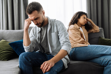 Quarrel between a couple in love. An upset guy and a girl are offended and ignore each other while sitting on the couch, turning away in different directions