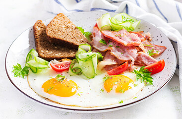 English breakfast - fried egg, bacon, tomatoes  and bread.