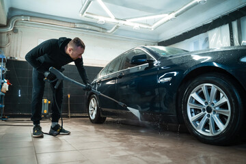 Fototapeta na wymiar Professional car wash. Detailing employee washes car with pressure washer