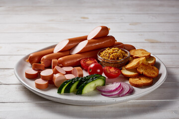 Sausages with vegetables and herbs garnish with sauces and bread on a gray ceramic plate on a white wooden table.