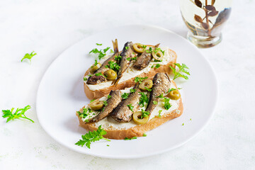 Sandwich - smorrebrod with sprats, green olives and butter on light table. Danish cuisine.