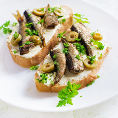 Sandwich - smorrebrod with sprats, green olives and butter on light table. Danish cuisine.