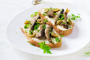 Sandwich - smorrebrod with sprats, green olives and butter on light table. Danish cuisine.
