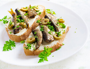 Sandwich - smorrebrod with sprats, green olives and butter on light table. Danish cuisine.