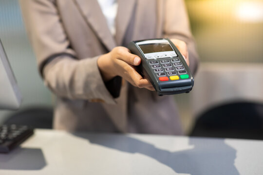 Female receptionist employee holding card reader machine on hand at checkout counter.