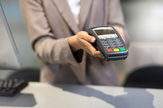 Female receptionist employee holding card reader machine on hand at checkout counter.