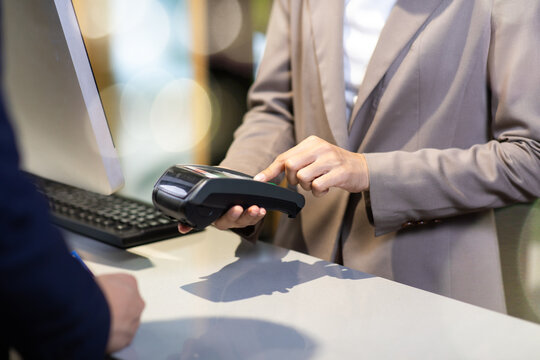 Female receptionist employee holding card reader machine on hand at checkout counter.
