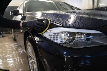 Fototapeta na wymiar Man cleans car body with disc sponge. Preparing auto for polishing. Detailed car wash