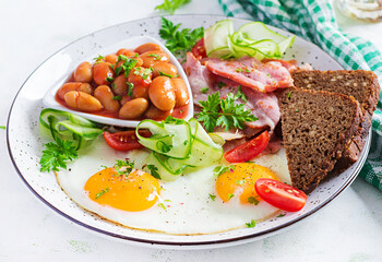 English breakfast - fried egg, beans, bacon, tomatoes  and bread.