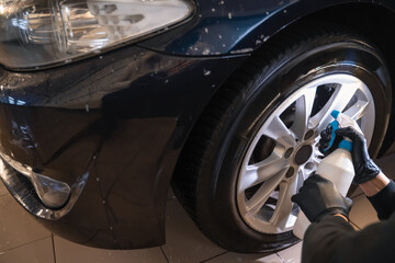 Fototapeta premium Car wash worker sprays wheel rim cleaner. Professional car detailing