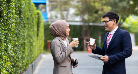 Young business muslim woman and business man colleague walking and discussing outside the office. Woman is holding a coffee and businessman is holding a digital tablet outdoor.