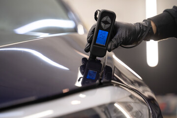 Detailing worker checks the condition of the paintwork with electronic thickness gauge. Car polishing concept