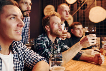Fans cheer and shout. Group of people together indoors in the pub have fun at weekend time