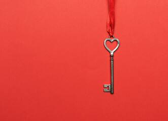 metal key hanging on a red ribbon, red background